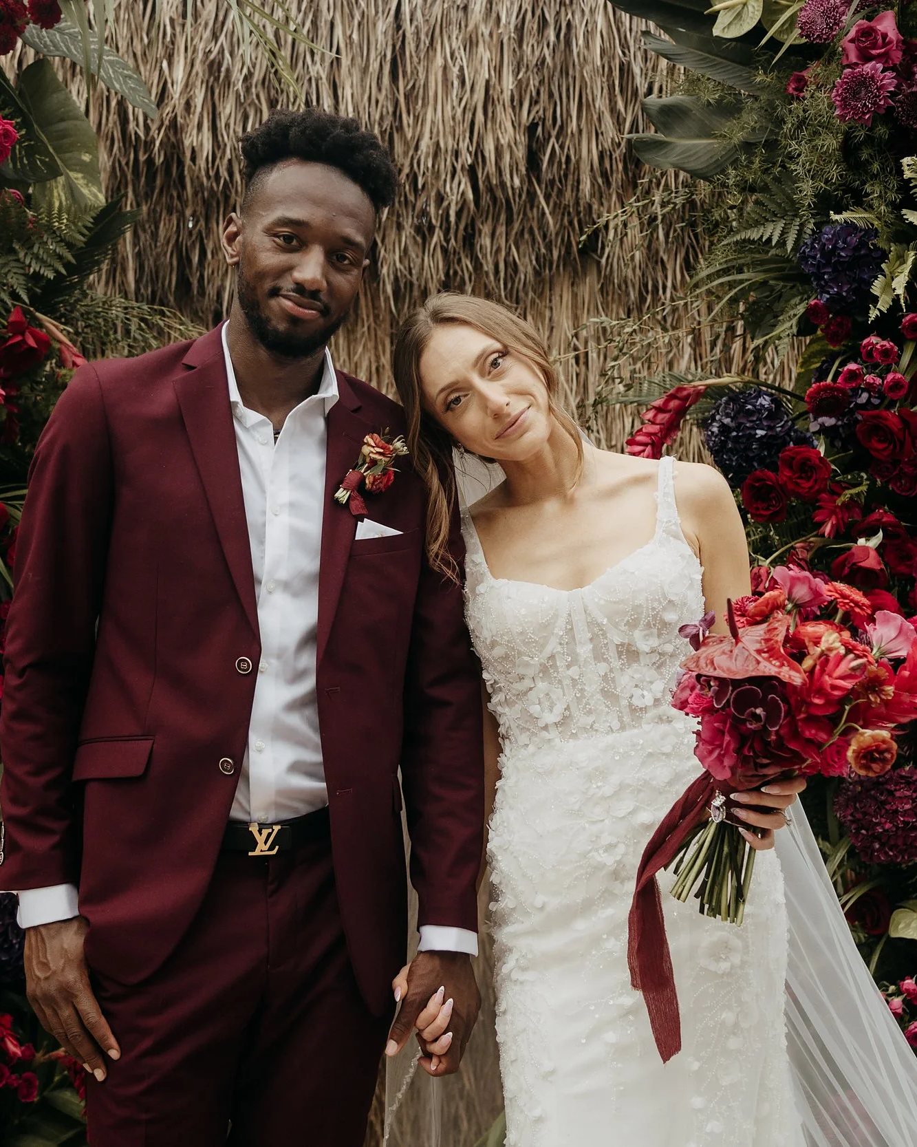 Bride and groom in front of a red floral wall
