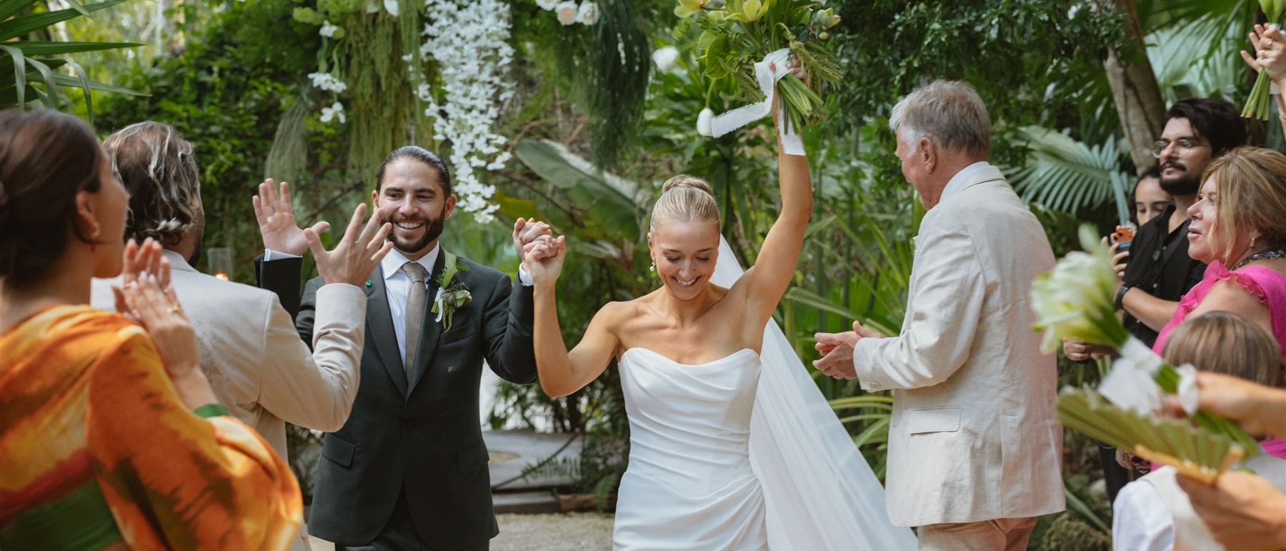 Newlyweds walking out of the jungle ceremony as their guests cheer